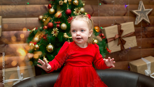 A girl in a red dress dances near the Christmas tree and fireworks.