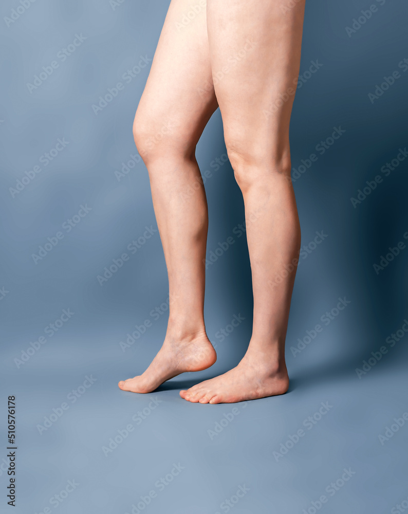 Female long bare legs on a gray background. Feet standing on toes. Spurs on the heels. Beauty salon, depilation, care, medicine, varicose veins, cosmetic surgery, spa. Female long bare legs on a gray background. Feet standing on toes. Spurs on the heels. Beauty salon, depilation, care, medicine, varicose veins, cosmetic surgery, spa.