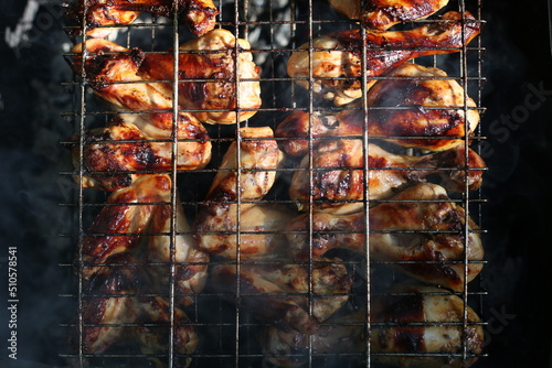 Chicken legs and wings are fried on coals in a brazier in a barbecue grill, marinated chicken is fried on a picnic