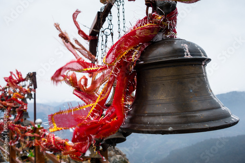 A closeup shot of hanging bells with holy red cloths with a snow covered mountains in the Background, Kartik Swami Temple, Rudraprayag Uttarakhand ,India. photo