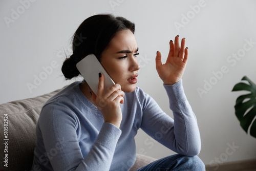 Portrait of irritated young woman arguing on phone. Outraged female talking angrily, shouting at cellphone. Customer support frustration concept. Copy space for text, white wall background, close up. photo