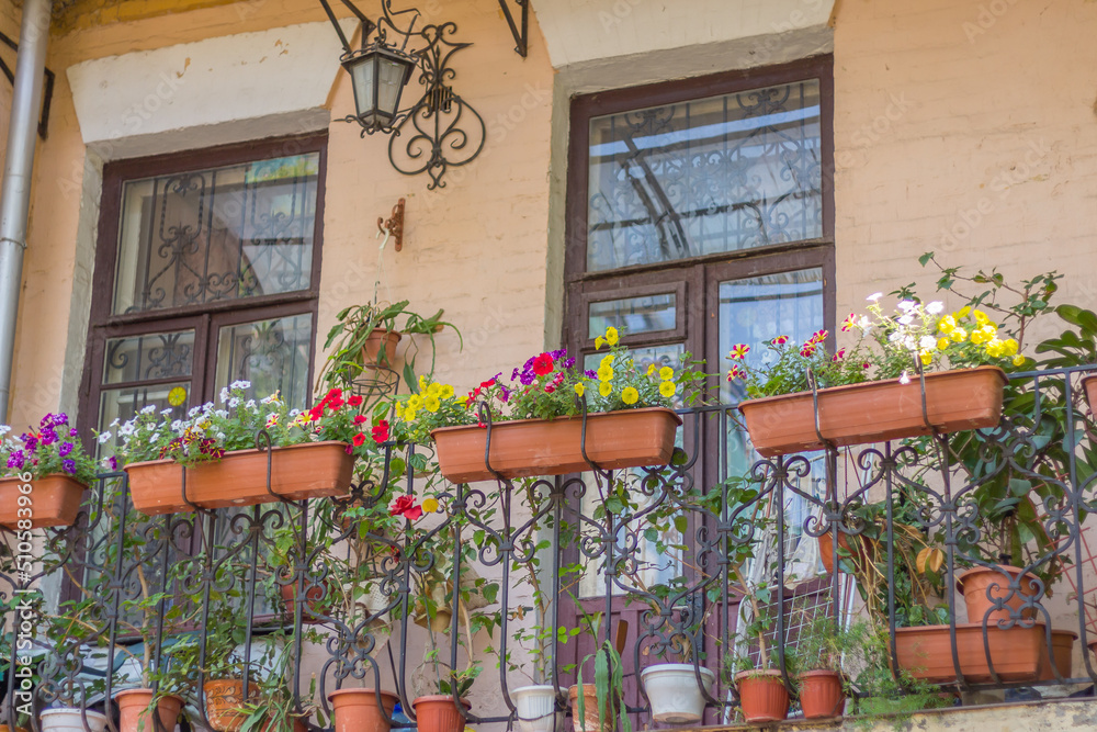 Balcony with flower pot and street lamp. Balcony design. Building facade decorated with flowers. Summer in the city. Apartment exterior with blooming plants. Summer cityscape.