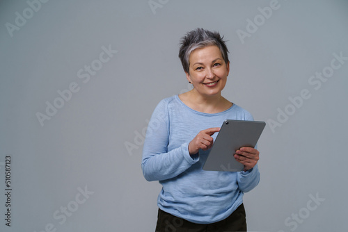 Mature grey haired businesswoman with digital tablet in hands working online. Pretty woman in 50s in blue blouse isolated on white. Older people and technologies