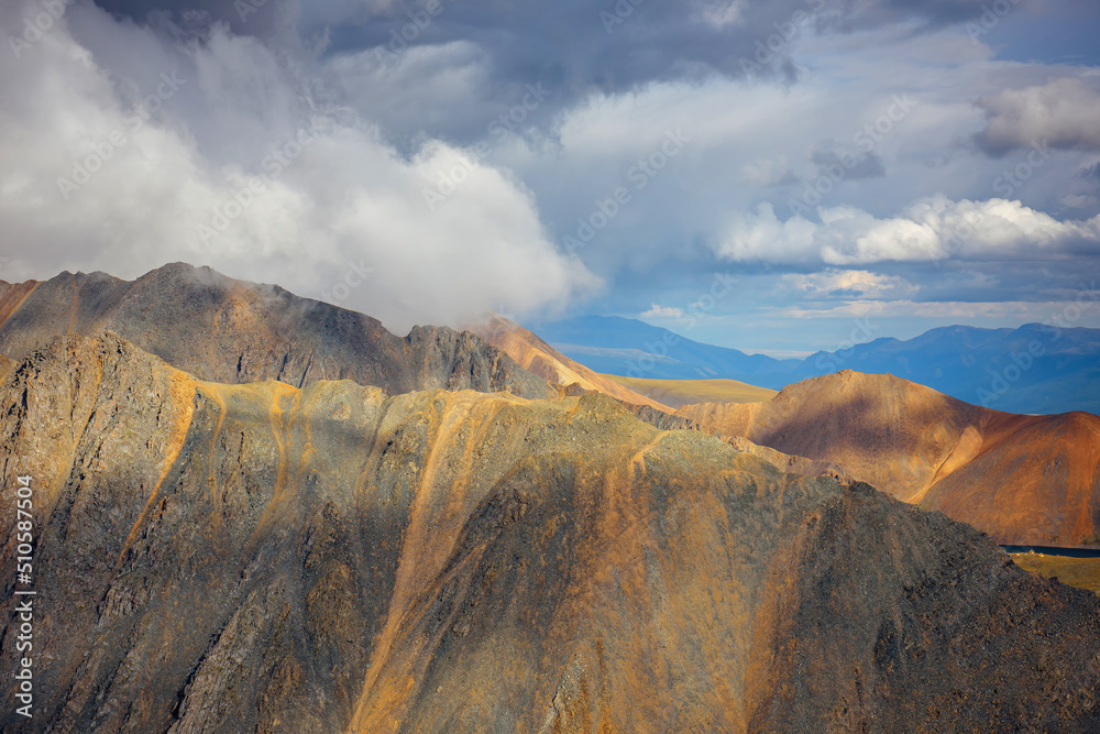 Colorful landscape of mountain peaks. Ridge of rocks under majestic cloudy sky, view from top. Altai, Siberia.