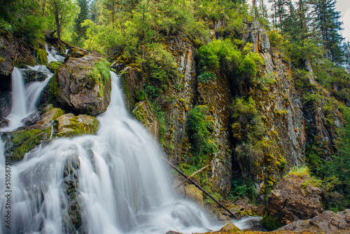 Picturesque waterfall in a mountain forest on sunny summer day. Lush greenery  trees and powerful falling water in the nature reserve. Beauty of the wild. Copy space.