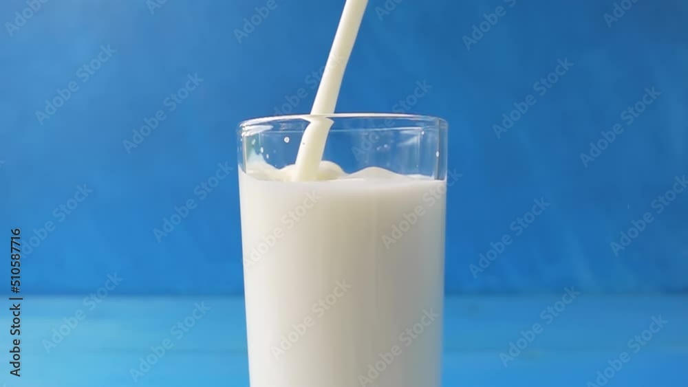 Milk is pouring into a glass with beautiful splashes close-up on a blue blurred background. 4k raw video with speed ramp effect. Filmed on high speed cinema camera. Milk is pouring into a glass with beautiful splashes close-up on a blue blurred background. 4k raw video with speed ramp effect. Filmed on high speed cinema camera.