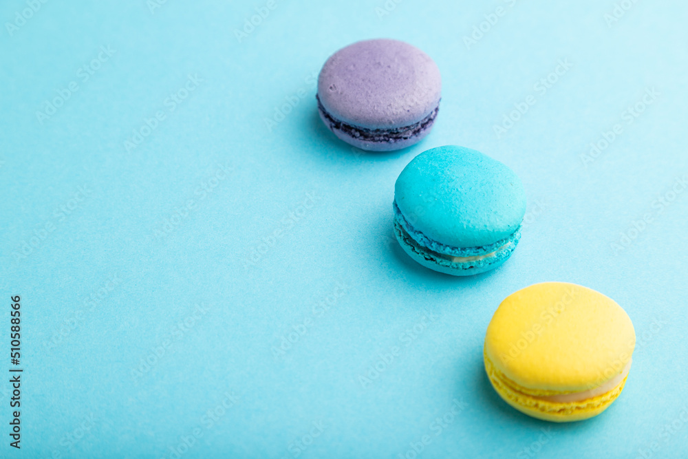 Obraz premium Yellow, purple and blue macaroons on blue pastel background. side view, copy space.