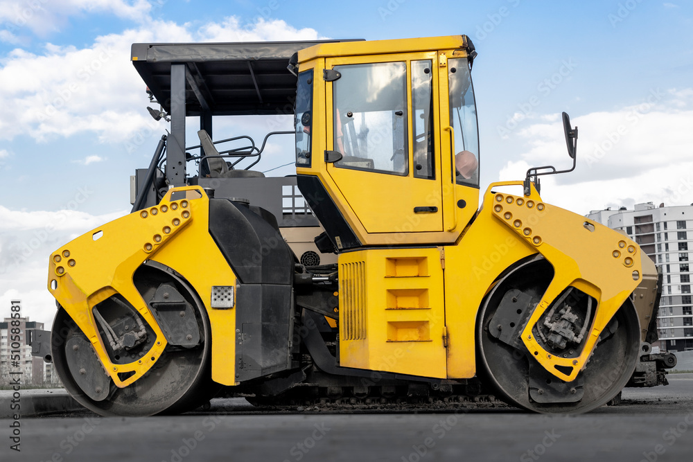 Asphalt paving machine and heavy vibratory roller close-up. A paver finisher, asphalt finisher or paving machine placing a layer of asphalt. Repaving the road surface. Road works.