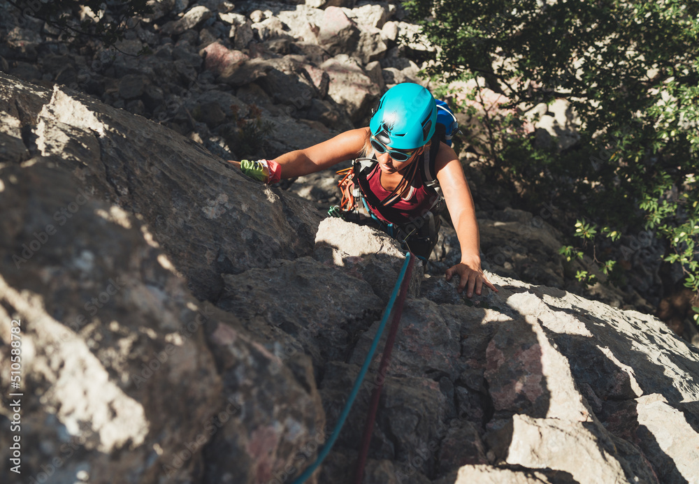 Obraz premium Active Woman in protective helmet and sunglasses on cliff rock wall lead climbing using rope and climbing harness in Paklenica National park, Croatia. Active extreme sports time spending concept photo