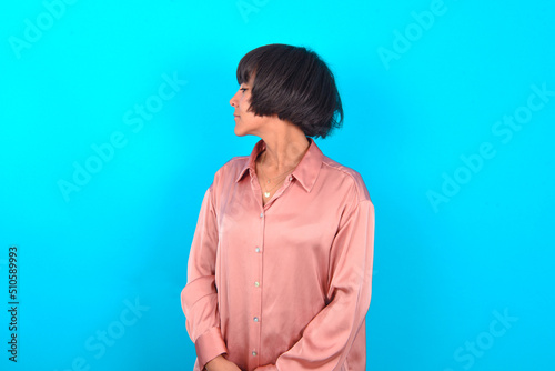 Side view of young happy smiling young brunette woman wearing pink silk shirt over blue background