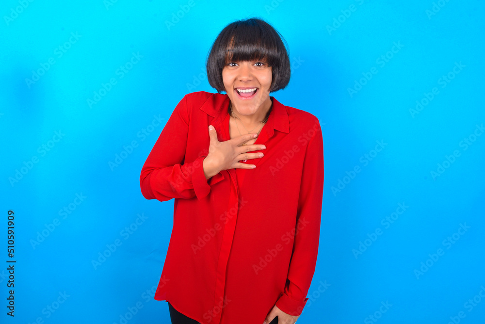 young brunette woman with short hair wearing red shirt over blue background smiles toothily cannot believe eyes expresses good emotions and surprisement young brunette woman with short hair wearing red shirt over blue background smiles toothily cannot believe eyes expresses good emotions and surprisement