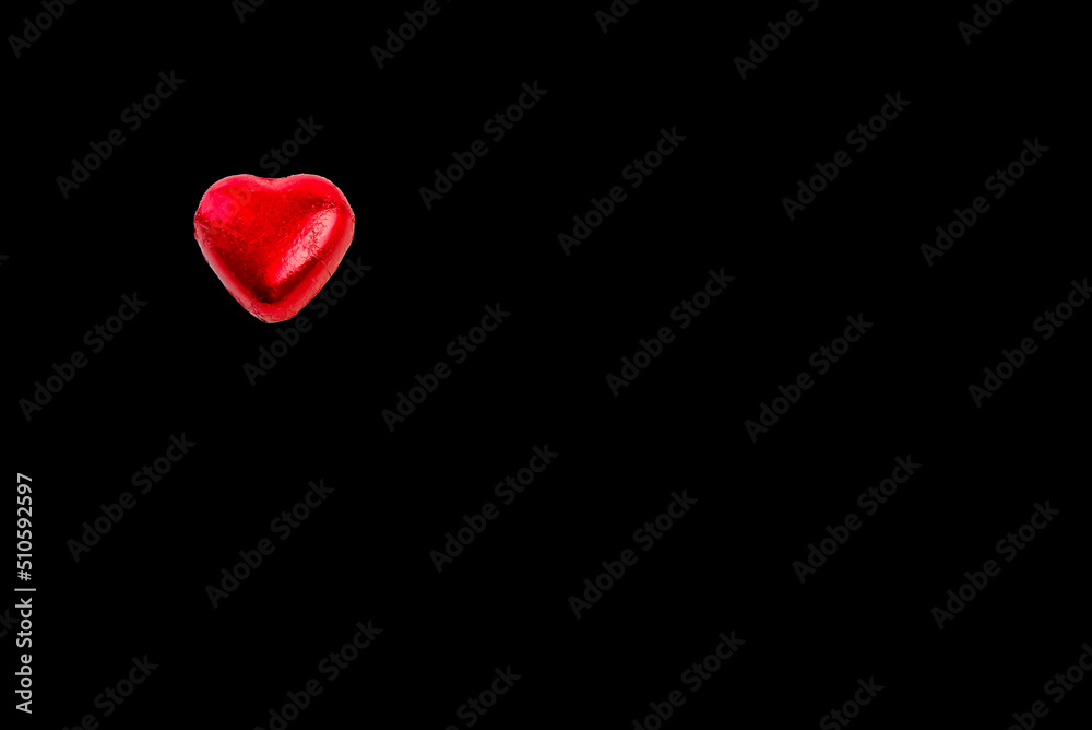Heart shaped chocolate bonbon wrapped in red foil on a black background Heart shaped chocolate bonbon wrapped in red foil on a black background