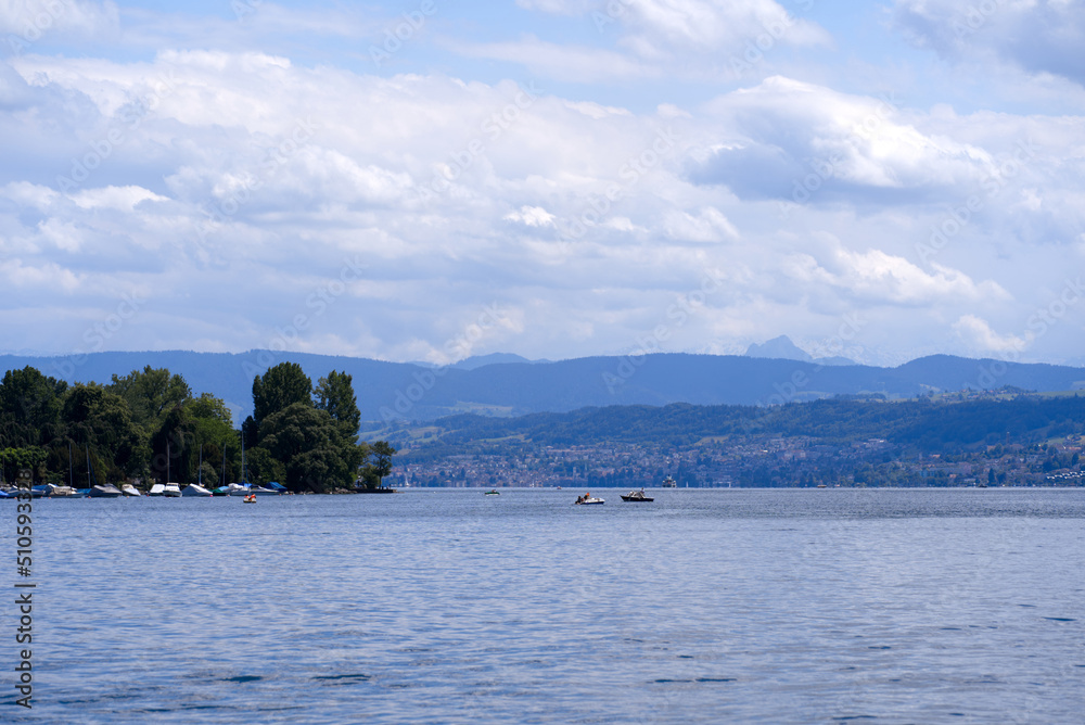 Scenic view over Lake Zürich at City of Zürich with mountains in the background on a blue cloudy spring day. Photo taken May 30th, 2022, Zurich, Switzerland. Scenic view over Lake Zürich at City of Zürich with mountains in the background on a blue cloudy spring day. Photo taken May 30th, 2022, Zurich, Switzerland.