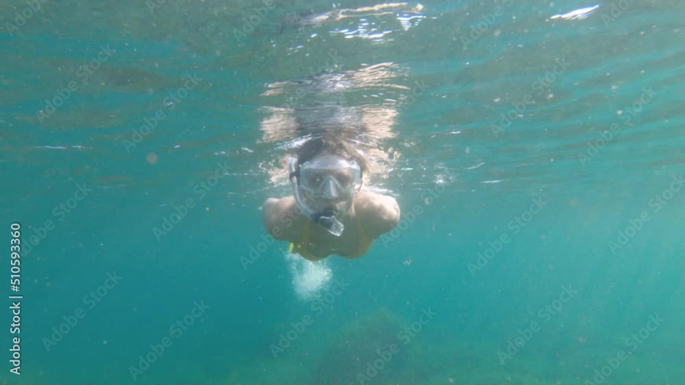 Attractive caucasian young woman in an underwater mask and snorkel dives underwater in the transparent waters of the ocean at shallow depth Attractive caucasian young woman in an underwater mask and snorkel dives underwater in the transparent waters of the ocean at shallow depth