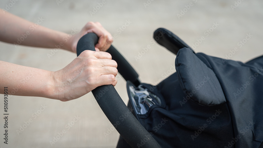 Action of a mother hand is holding and pushing on baby stroller or cart for walking on the road. Happiness parenthood concept scene.