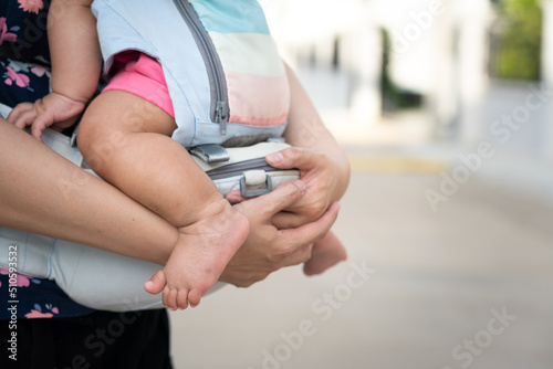 A mother is holding the baby by using baby carriage strap belt. Parenthood action scene photo. Selective focus.