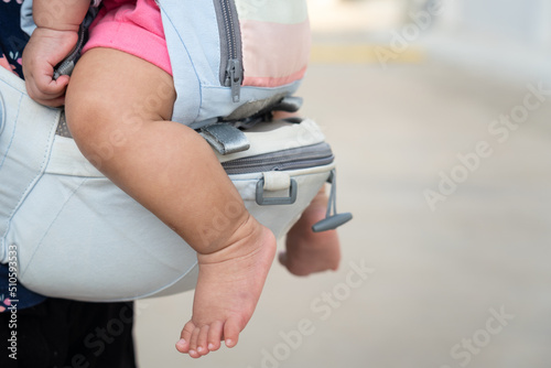 A mother is holding the baby by using baby carriage strap belt. Parenthood action scene photo. Selective focus.
