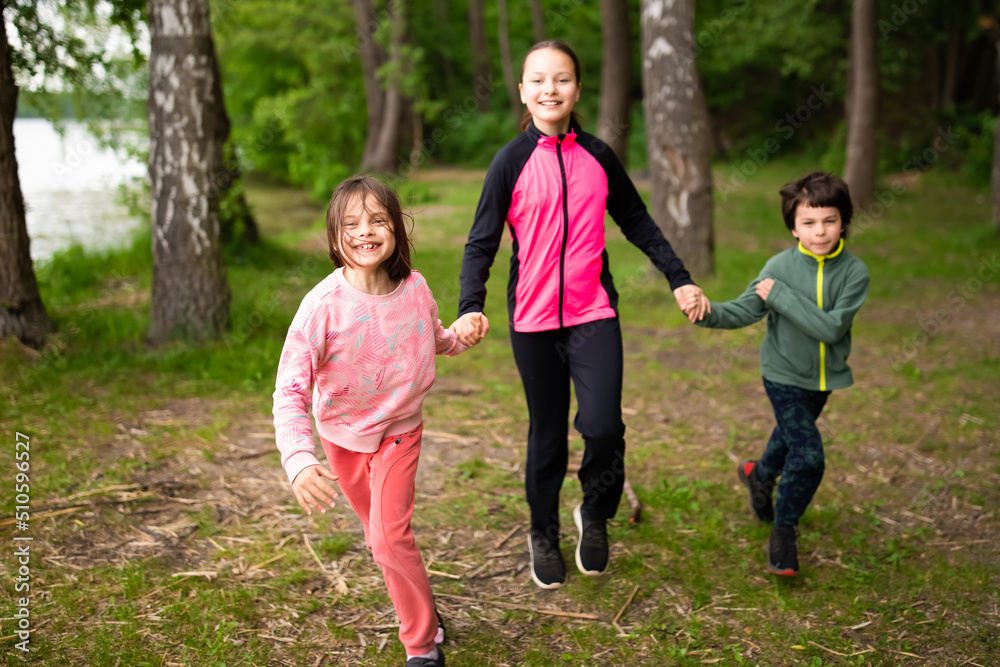 Three happy children running holding hands in forest outdoors
