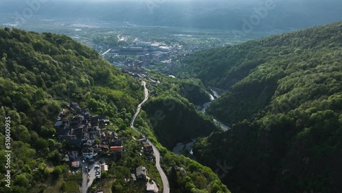 Flight above road through idyllic Italian village in alp valley hillside; drone photo