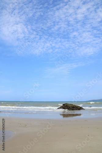 Soft focus of the waves beat at the beach with sand, rock, and blue sky with reflection in summer morning. Nature background concept.