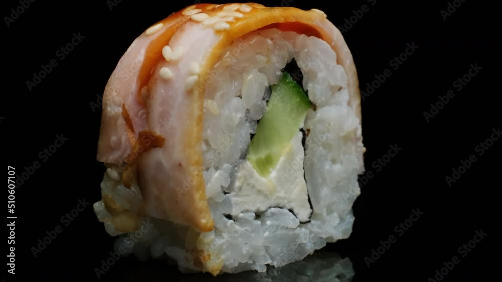 Sushi roll rotating on black background on mirrored table close-up. Fresh roll with bacon, cream cheese, cucumber, rice, sesame seeds. Sushi menu, Japanese food.