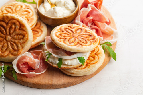 Italian sandwich. Tigella, prosciutto, italian crudo ham, soft cheese and rocket salad. Tigelle are thin round breads from the Emilia-Romagna, Northern Italy food. Close-up. photo