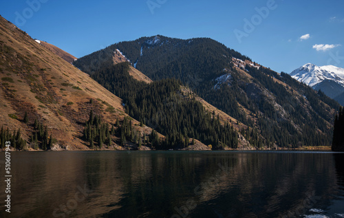 Autumn mountains in haze morning light reflected in calm waters of green lake. Majestic mountains. Mountain lake water landscape scene.