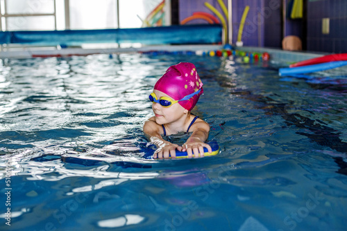 Child schoolgirl learns to swim with board in pool. Swimming lesson. Active child plays in water