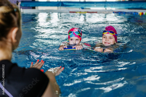Canvas Print Children learn to swim with board in pool under guidance of coach