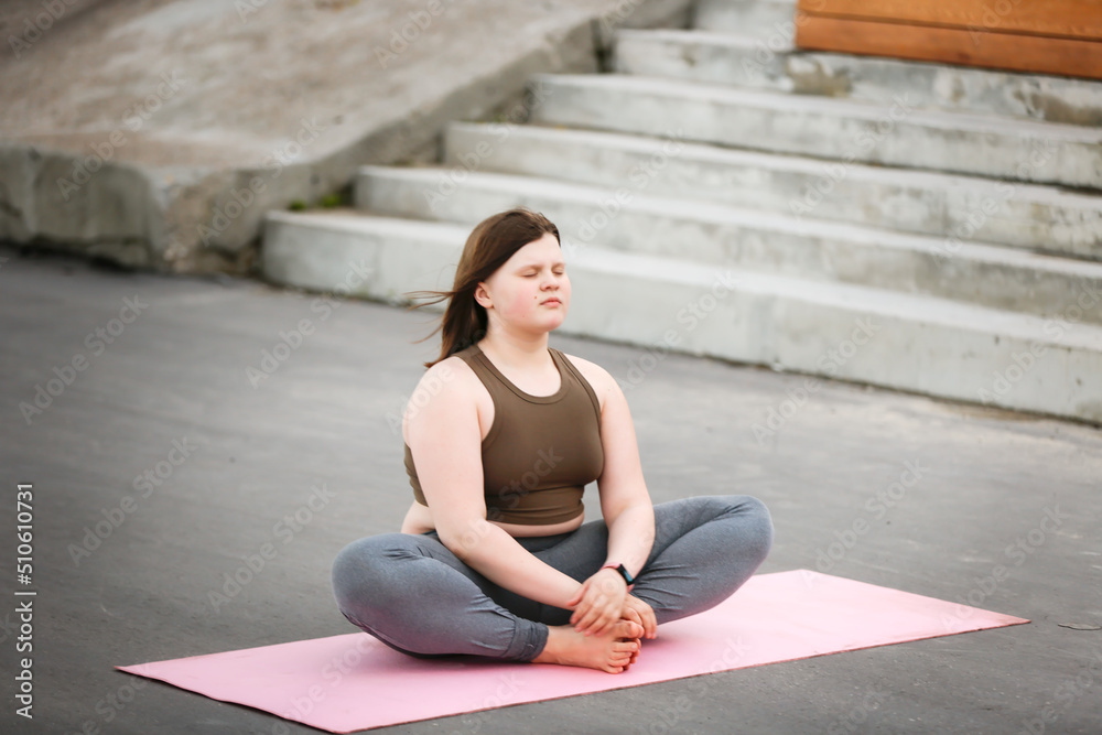 Plus size girl teenager meditates on yoga mat outside in summer, excess weight in teenagers, calmness and yoga classes