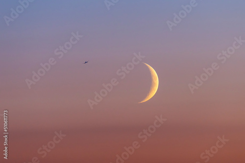 An airplane flying near the young crescent of the moon