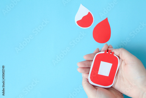 hand holding bloody bag shape made from paper on blue background, copy space, top view. blood donation concept, world blood donor day