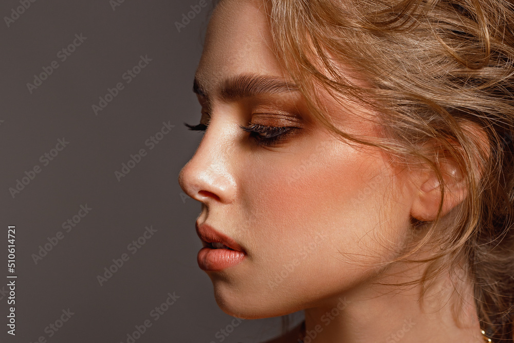 Beauty young girl in profile with perfect smooth skin and makeup with wavy hair looks away on a gray background, skin care, cosmetology Beauty young girl in profile with perfect smooth skin and makeup with wavy hair looks away on a gray background, skin care, cosmetology