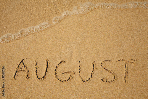 August - handwritten on the soft beach sand.