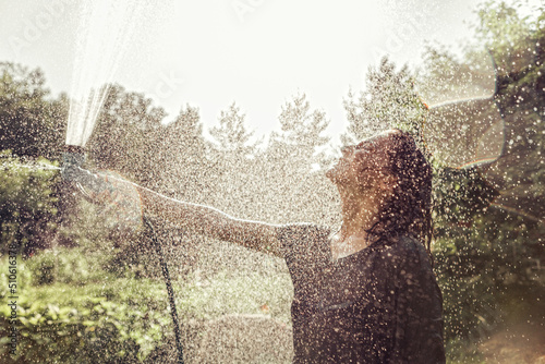 Concept. Summer, heat. A woman sprays herself with a garden hose. Splashes, drops, defocus.