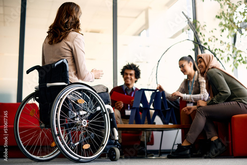 Rear view of businesswoman in wheelchair and her colleagues talk on break in the office. photo