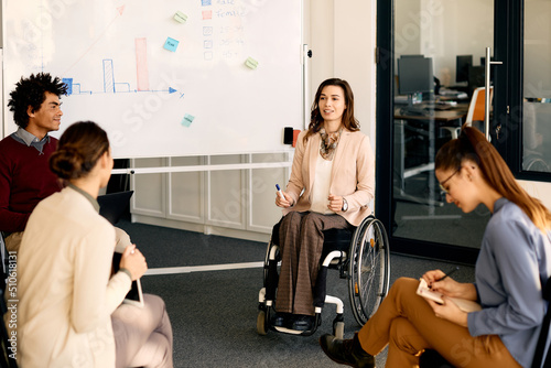 Female CEO in wheelchair talks to her colleagues while holding presentation in the office. photo