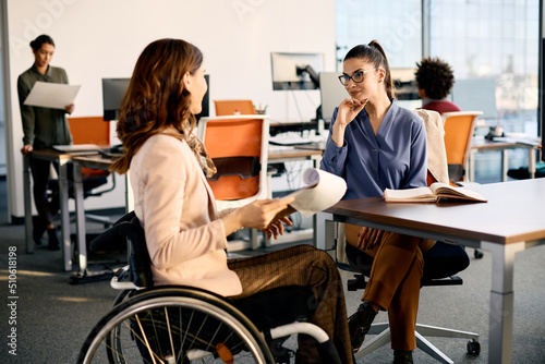 Happy businesswoman and her colleague in wheelchair talk while working in office.