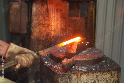 Foto Professional male blacksmith forming red hot metal on an anvil in interior blacksmith workshop