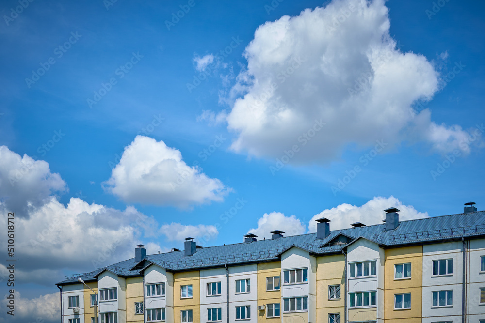 Part of a residential building with a roof against a blue sky covered with white clouds Part of a residential building with a roof against a blue sky covered with white clouds
