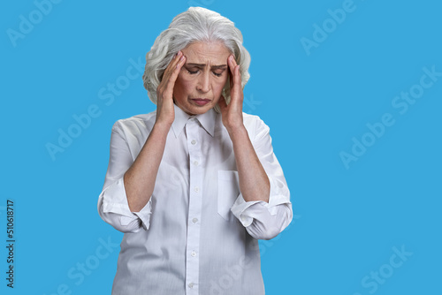 Overworked senior woman suffering from headache against blue background. Health problem concept.