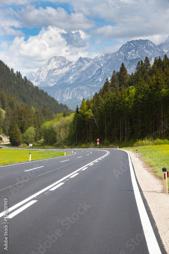 Asphalt road among green meadows with bavarian alps on background.