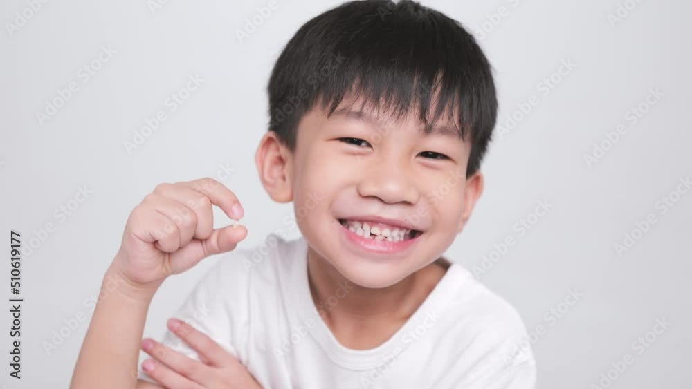 Asian kid holding the first fallen baby milk teeth while the second tooth loses and bends in his mouth. A happy boy proudly smiles at his dental care. Asian kid holding the first fallen baby milk teeth while the second tooth loses and bends in his mouth. A happy boy proudly smiles at his dental care.