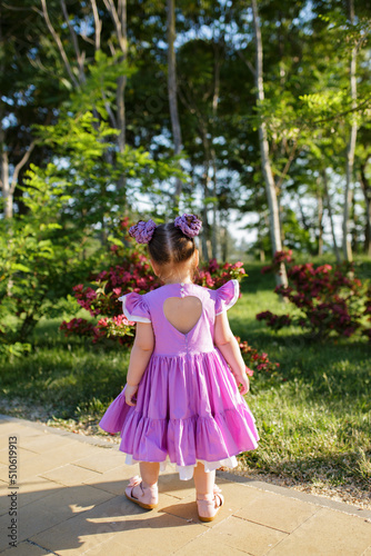 Rear view of a little child girl in summer dress walking in green park
