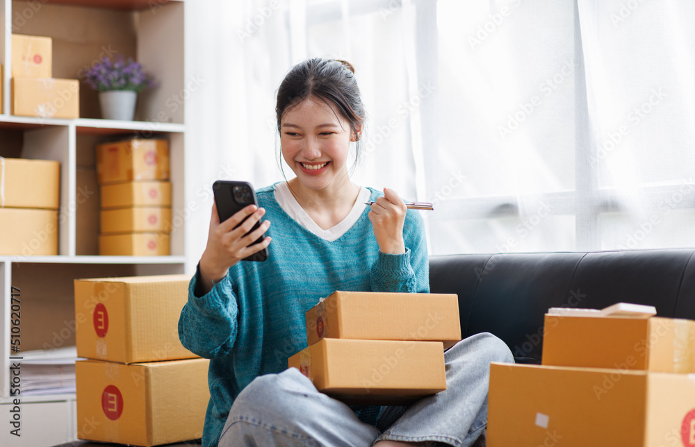 Asian business woman on sofa using a laptop computer checking customer order online shipping boxes at home. Starting SME Small business entrepreneur freelance. Online business, SME Work home concept. Asian business woman on sofa using a laptop computer checking customer order online shipping boxes at home. Starting SME Small business entrepreneur freelance. Online business, SME Work home concept.