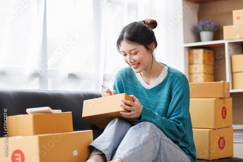 Asian business woman on sofa using a laptop computer checking customer order online shipping boxes at home. Starting SME Small business entrepreneur freelance. Online business, SME Work home concept.