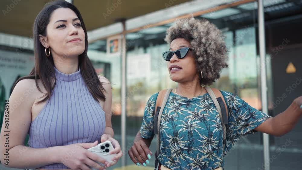 Two handsome multiethnic women talking and hailing a taxi on the bus station outdoors
