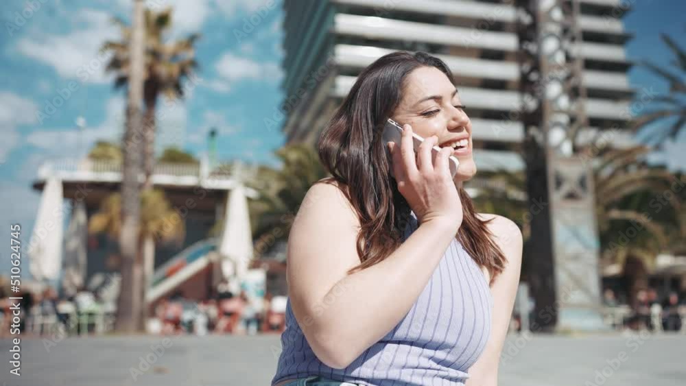 Laughing brunette woman talking by mobile while sitting on the bench outdoors Laughing brunette woman talking by mobile while sitting on the bench outdoors