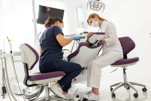 Dentist and assistant examining kid mouth with dentistry equipment instrument. Teeth treatment for children. Stomatology and orthodontology photo