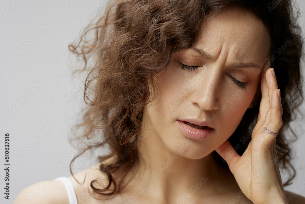 Closeup portrait of suffering from headache, sad curly beautiful woman in basic white t-shirt touches head close eyes posing isolated on white background. People Emotions Lifestyle concept. Copy space Closeup portrait of suffering from headache, sad curly beautiful woman in basic white t-shirt touches head close eyes posing isolated on white background. People Emotions Lifestyle concept. Copy space
